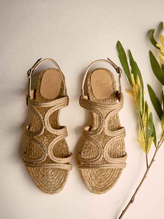 Geflochtene Sandalen aus Naturmaterial mit breiten Riemen, offener Zehenpartie und flacher Sohle in warmem Beigeton.
