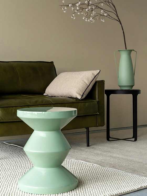 Mintfarbener Beistelltisch vor grünem Sofa mit Vase und Zweigtisch.