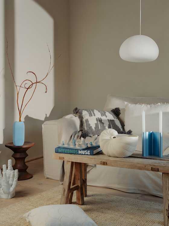 Helles Wohnzimmer mit Sofa, Holzbank, Dekoobjekten und Pendelleuchte.