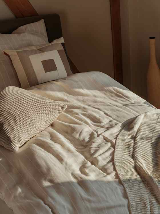 Gemütliches Bett mit heller Bettwäsche im warmen Licht.