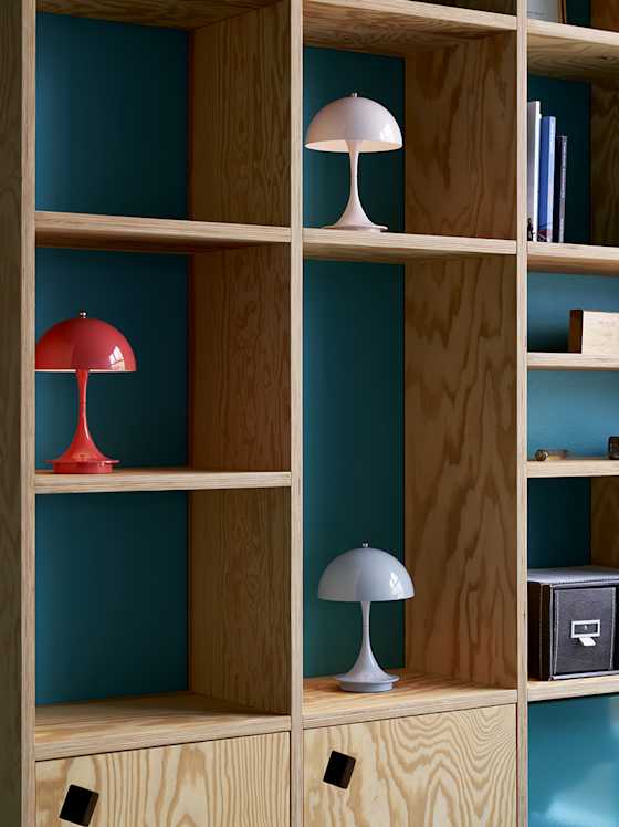 Holzregal mit farbigen Design‑Tischleuchten und Büchern.