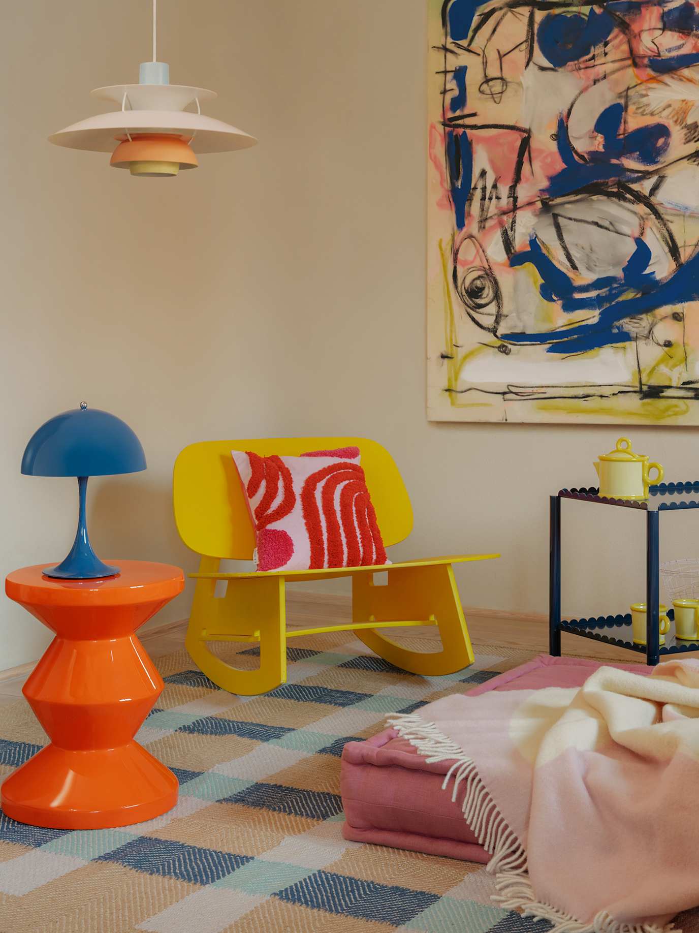 Farbenfrohes Wohnzimmer mit gelbem Sessel, orangefarbenem Beistelltisch, blauer Lampe und abstraktem Wandbild.