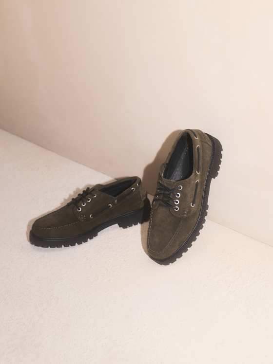 Olivegrüne Wildleder‑Schnürschuhe mit robuster Profilsohle, lässig arrangiert auf hellem Untergrund.