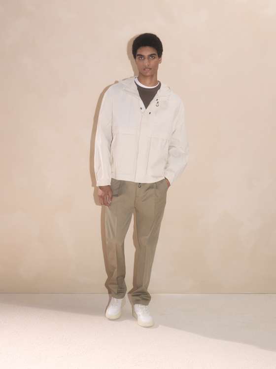 Weiße Funktionsjacke, kombiniert mit T‑Shirt, olivfarbener Stoffhose und weißen Sneakern.