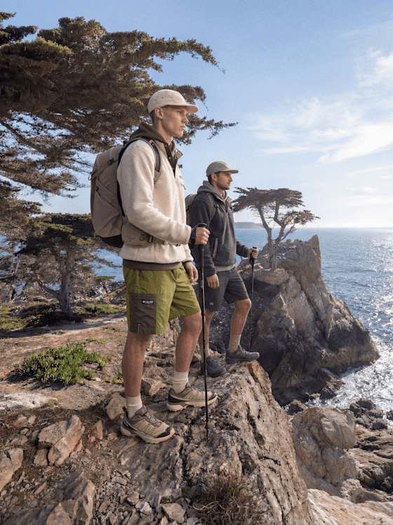 Zwei Wanderer im Outdoor-Look auf einer Klippe am Meer
