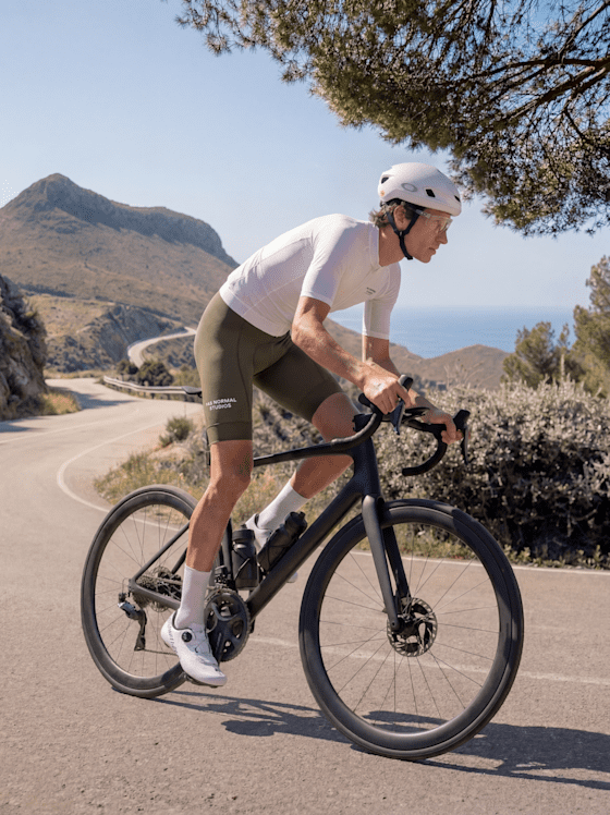 Rennradfahrer auf einem Bike mit grüner Bib-Shorts, weißem Trikot und weißem Helm bei einer Abfahrt